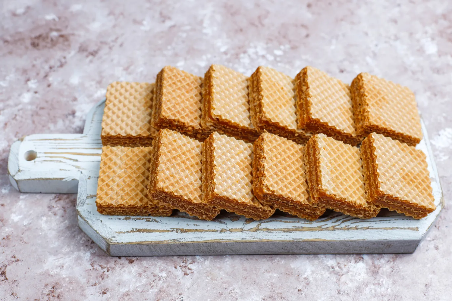 Galletas de oblea apiladas en una tabla de madera, mostrando su textura crujiente y color dorado. Ideal para acompañar café o té.